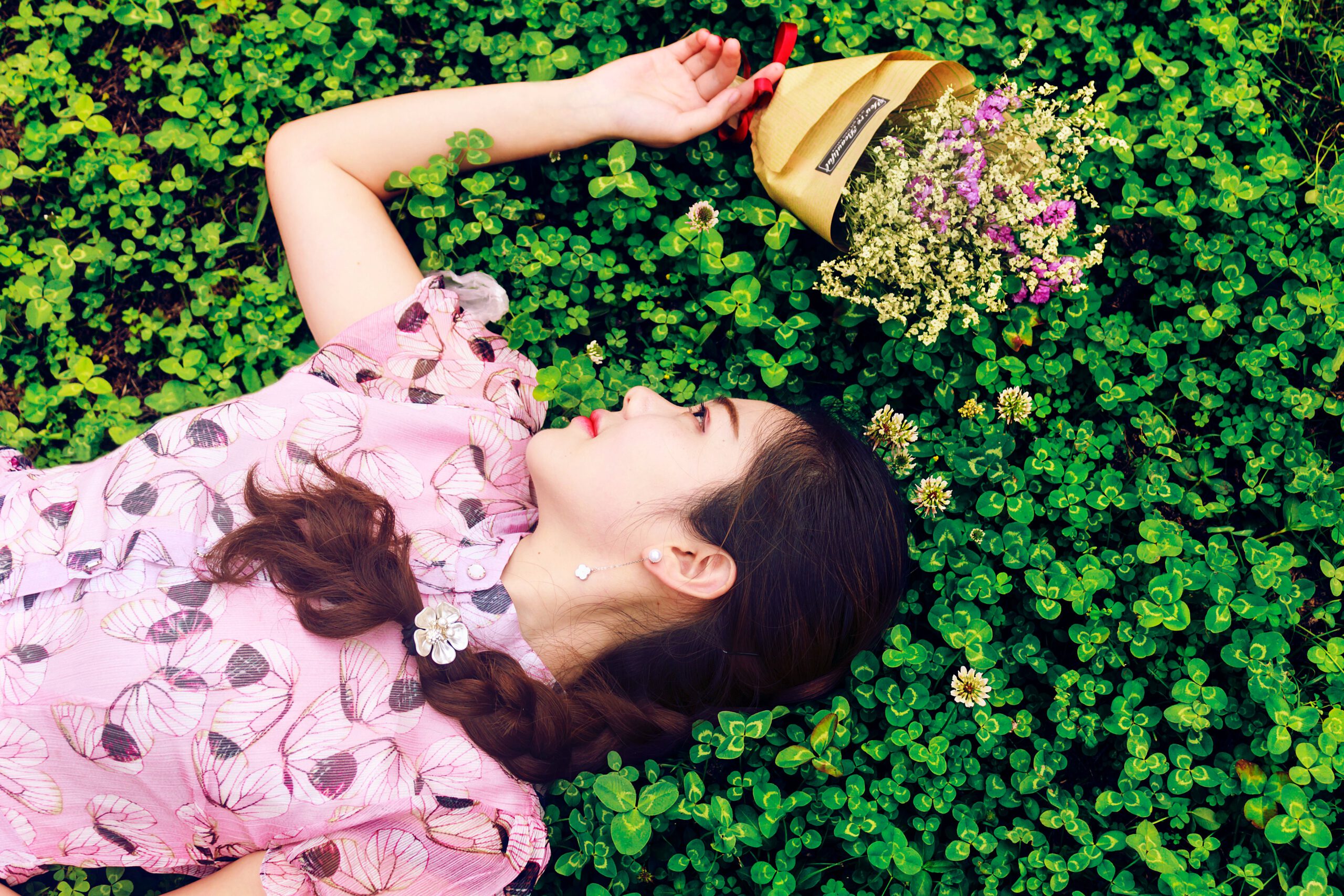 Kobieta leżąca na trawie w otoczeniu kolorowych kwiatów w różowej zwiewnej sukience