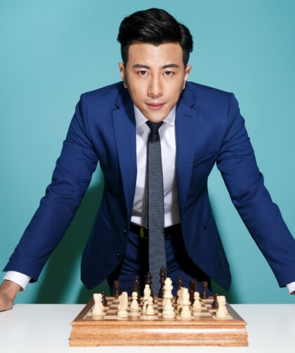Mężczyzna ubrany w stylu biznesowym, stojący nad stołem z rozłożonymi szachami